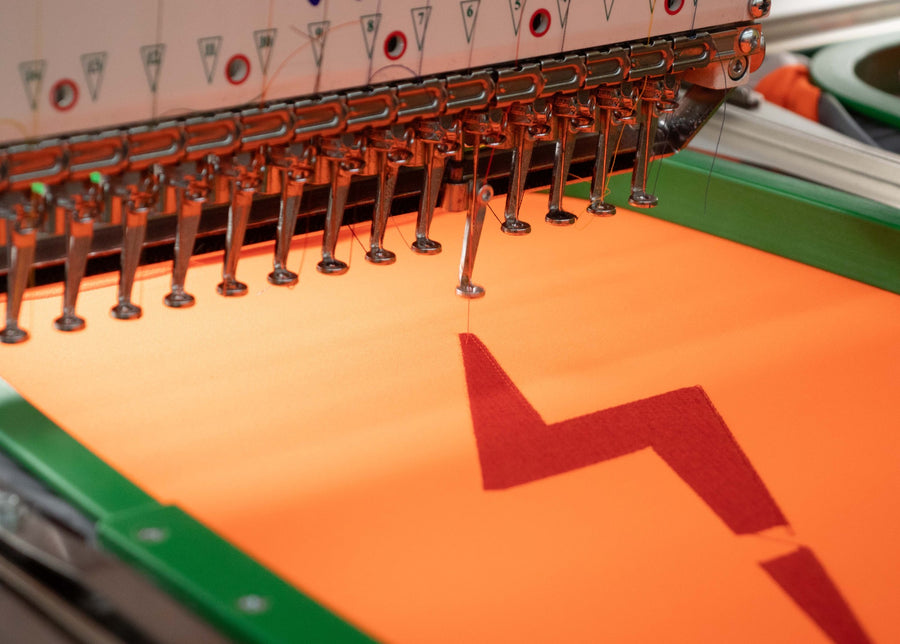 Multi-needle embroidery machine stitching a logo onto hi vis fabric at the Mr. Loriku shop